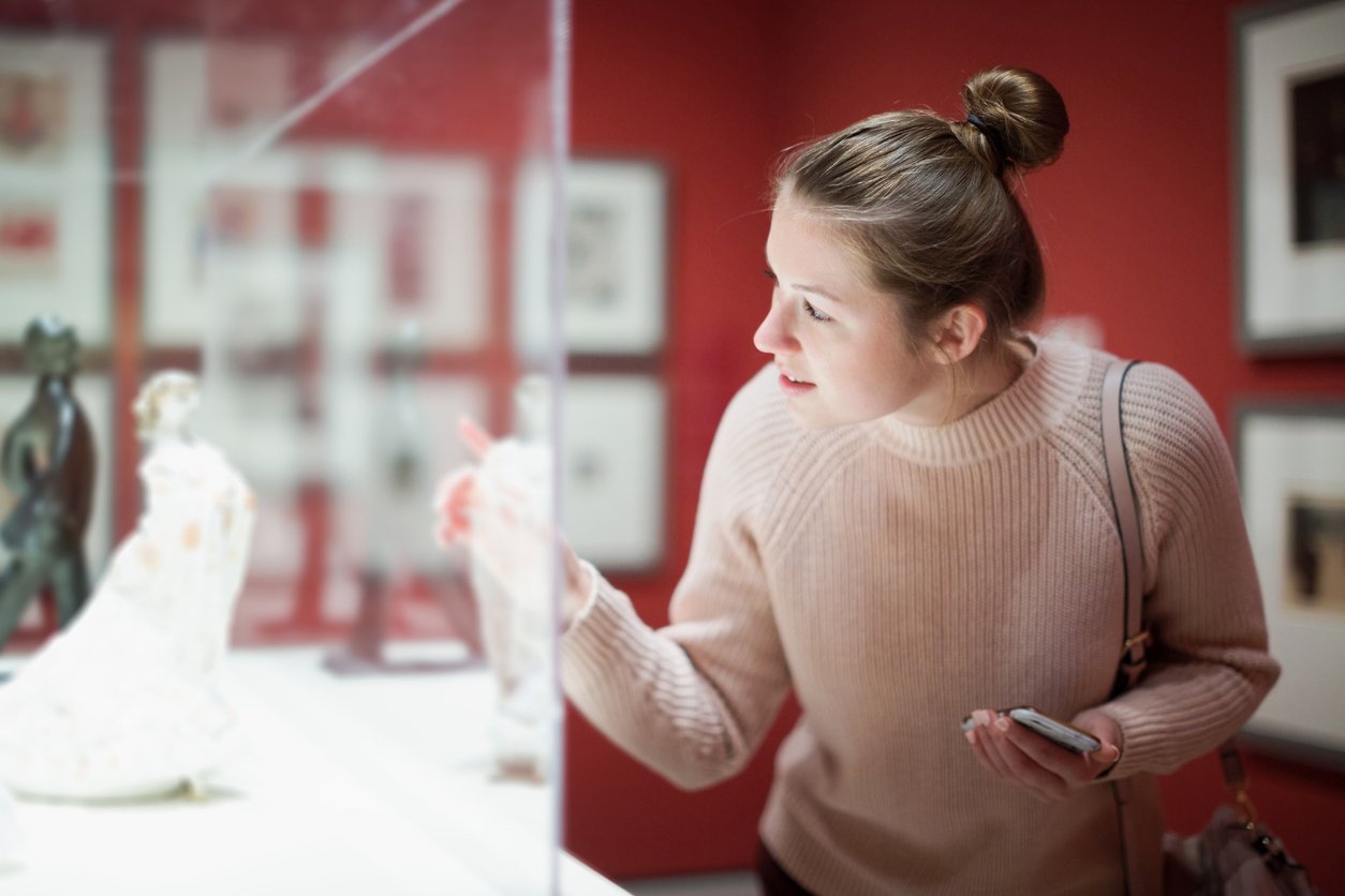 Young woman visitor using phone in museum